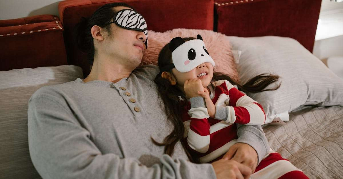 A father and daughter wearing sleep masks relax on a cozy bed, enjoying a moment together.