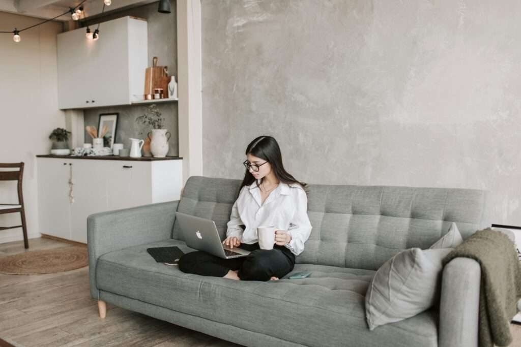 Woman in a modern living room working on a laptop and enjoying a coffee.